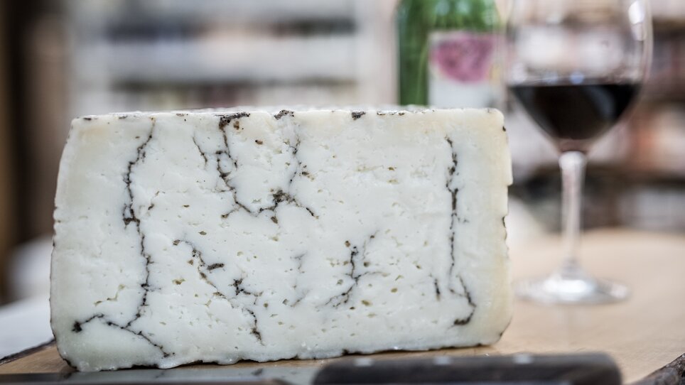 A piece of cheese, alongside a glass of red wine and a bottle. | © Nussbaumer