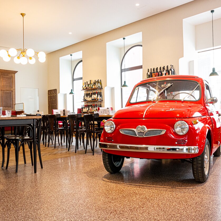 Der Steirer I Mangiare e bere a Graz | © Florian Weitzer Hotels & Restaurants Un'auto rossa si trova nel ristorante Der Steirer a Graz, circondata da tavoli e sedie. | © Florian Weitzer Hotels & Restaurants
