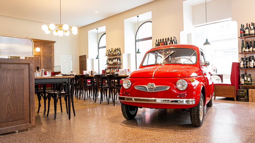 A red car stands in Restaurant Der Steirer in Graz, surrounded by tables and chairs. | © Florian Weitzer Hotels & Restaurants