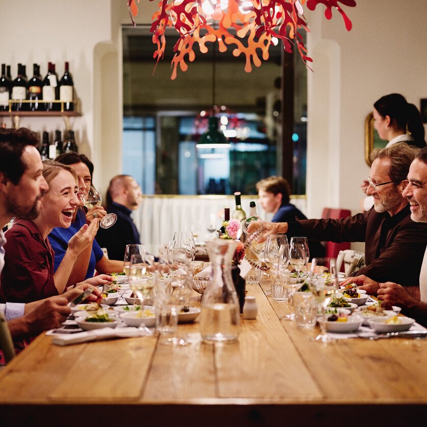 Gli ospiti siedono a un lungo tavolo nel ristorante “Der Steirer” e si godono il cibo e le bevande. | © Florian Weitzer Hotels & Restaurants