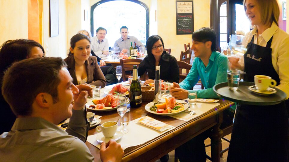 Social dining in a restaurant with guests and a waitress. | © Don Camillo