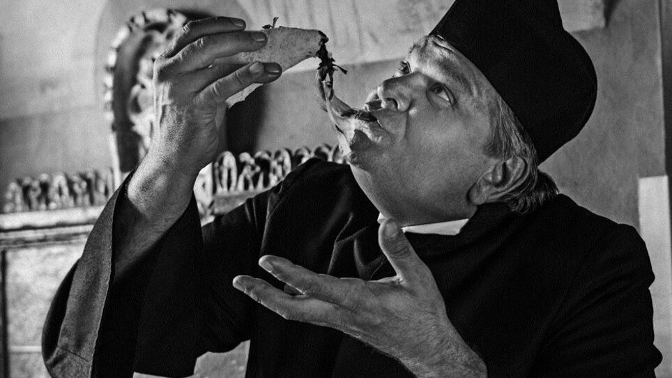 A man in black attire enjoys a meal - the photo is in black and white. | © Don Camillo