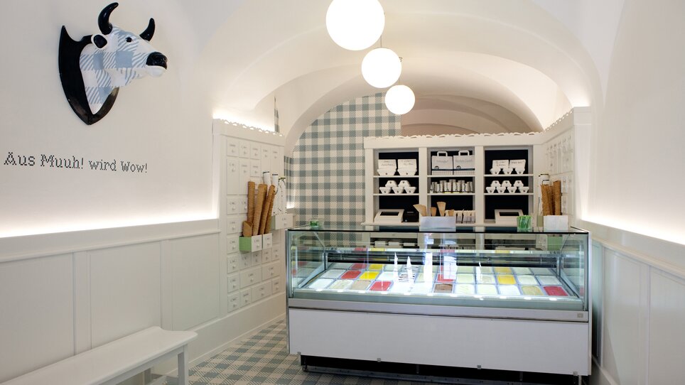 Interior of the ice cream shop featuring colorful ice cream and cow sculpture. | © Eis Greissler 
