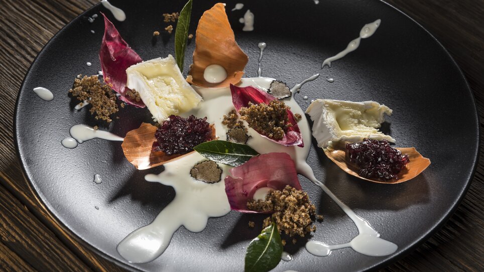 Ein kunstvoll angerichteter Teller mit Käse, Blütenblättern und Sauce. | © El Pescador - Werner Krug