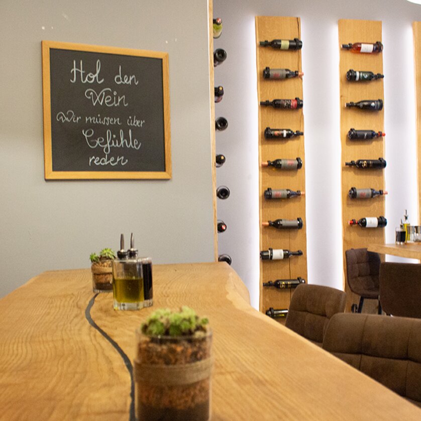 A restaurant in Graz featuring a wine rack and wooden bar. The board reads: 'Get the wine, we need to talk about feelings.' | © eleven - idlab Media