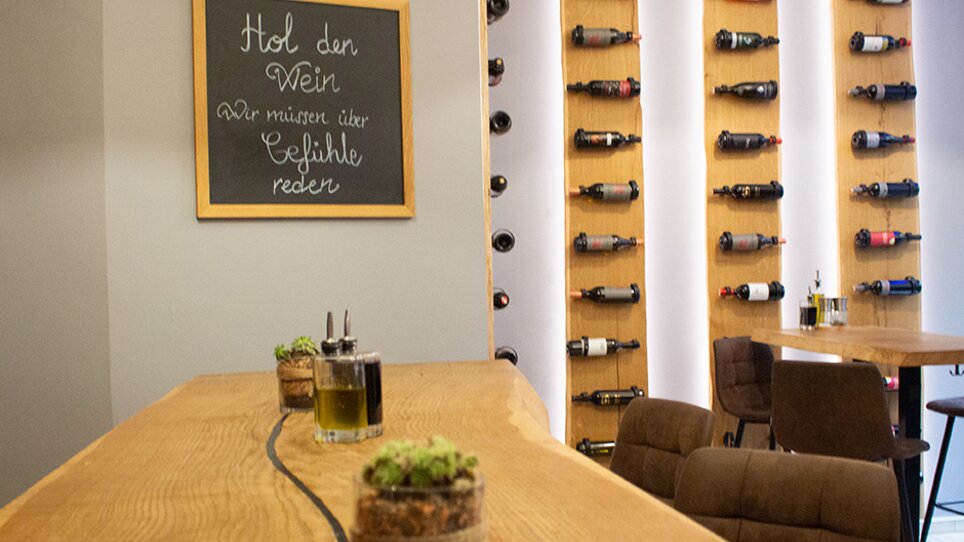 A restaurant in Graz featuring a wine rack and wooden bar. The board reads: 'Get the wine, we need to talk about feelings.' | © eleven - idlab Media