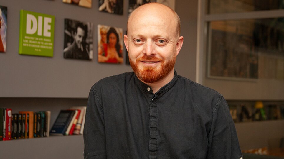 A man with a red beard and shirt in a modern room. | © eleven - idlab Media