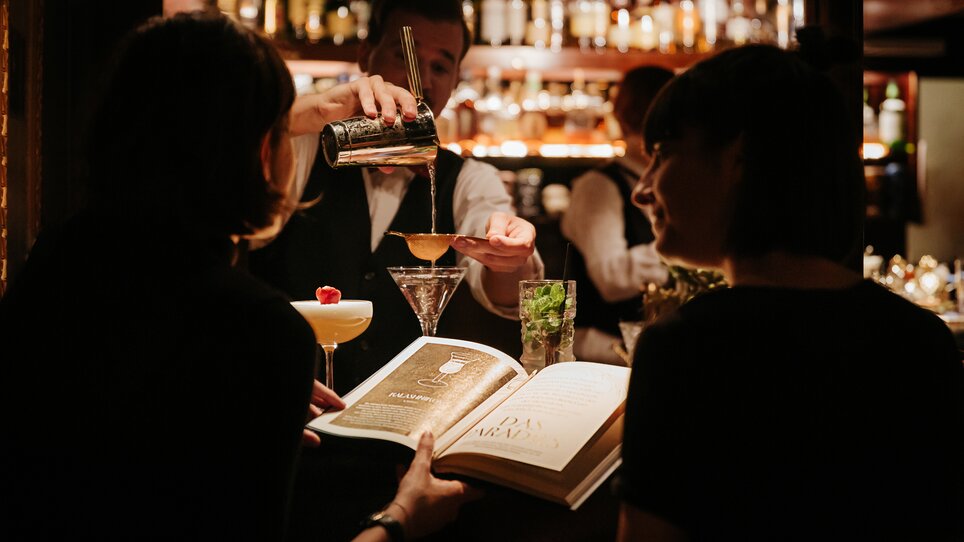 Due ospiti al bar mentre un barista prepara cocktail. | © Daniel Kindler