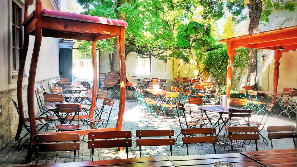 Gemütlicher Gartenbereich mit Tischen und Stühlen unter Bäumen. | © Eschenlaube