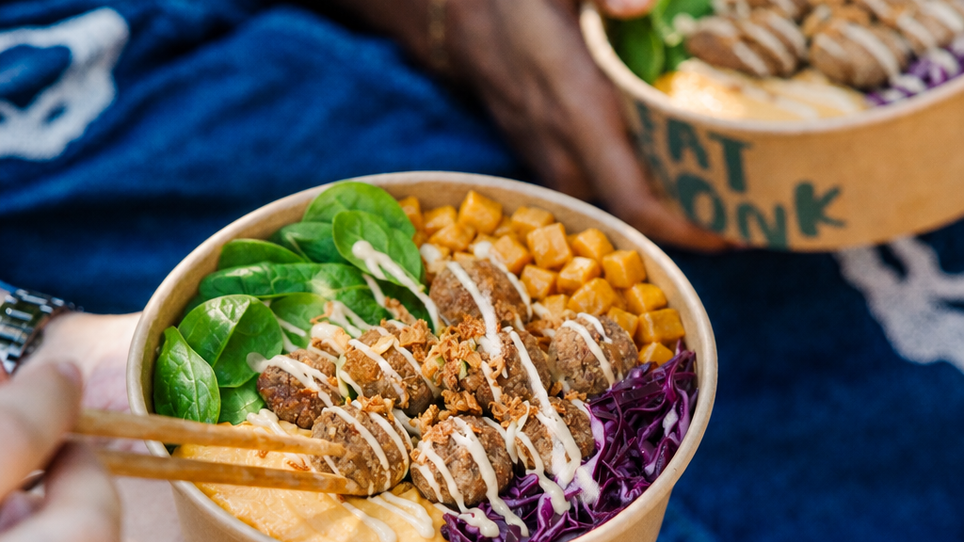 Zwei Personen halten Bowls mit gesundem Essen, darunter Salat, Falafel und ein Dressing. | © Fat Monk – Deli Bowls