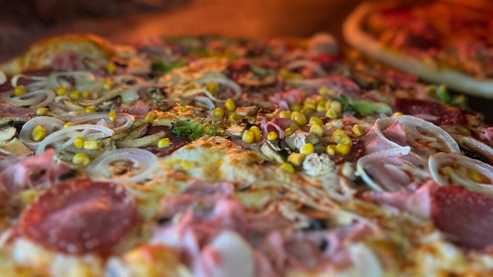 Deliziosa pizza cotta in forno a legna, con fuoco sullo sfondo. | © Forno Antico