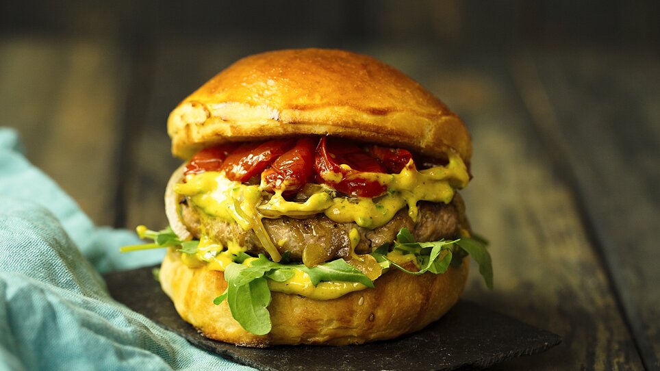 Hamburger succulento con insalata, pomodori e salse su un tagliere di legno. | © TG-Graphics
