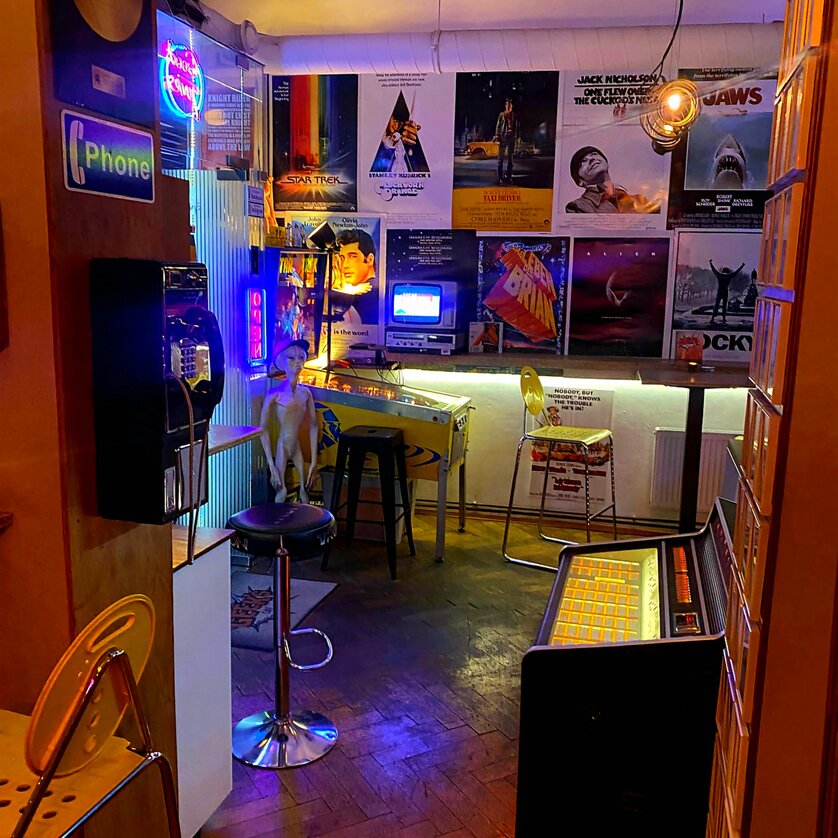 Cozy café with retro charm, neon lights, and movie posters. | © Geek’s Retro Café-Bar
