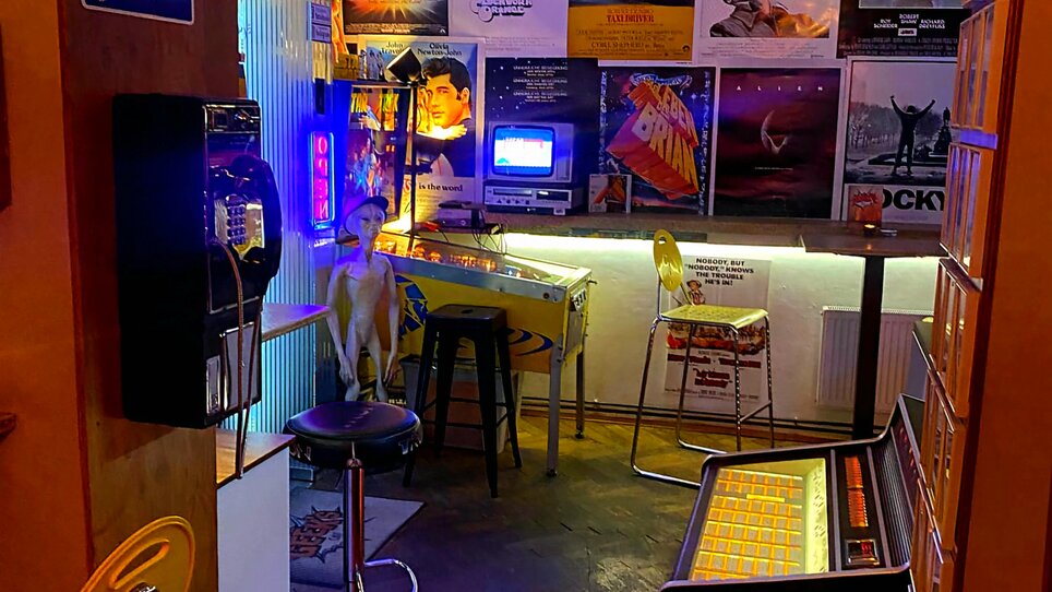 Cozy café with retro charm, neon lights, and movie posters. | © Geek’s Retro Café-Bar