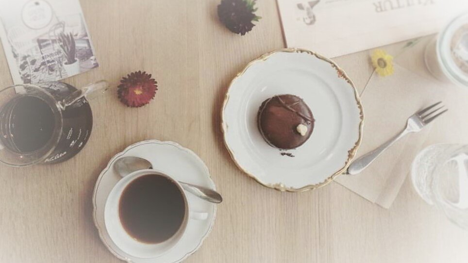 Schwarzer Kaffee und Süßgebäck auf einem Tisch, umgeben von Blumen. | © Cafe Greenhouse