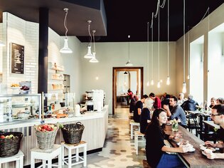 Moderne Café-Atmosphäre mit Gästen, frischen Früchten und Holzinterieur. | © Lupi Spuma 