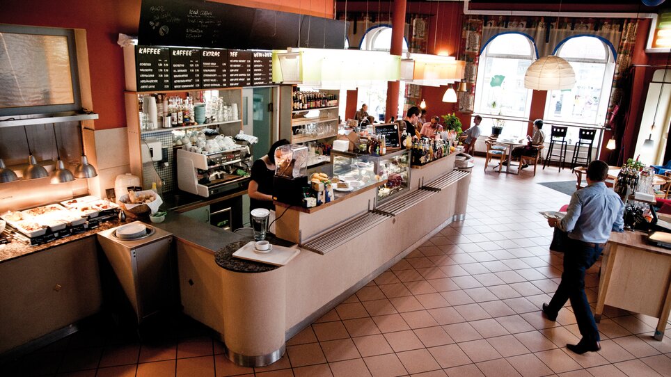 Gemütliches Café mit Theke, bei der Speisen und Getränke angeboten werden. | © Ginko - Udo Stelzer +
