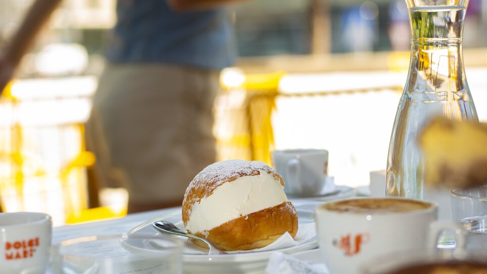 A maritozzo, a sweet Italian treat, on a table with coffee and water at the Grazie Roma restaurant in the Hotel Daniel in Graz. | © Florian Weitzer Hotels & Restaurants