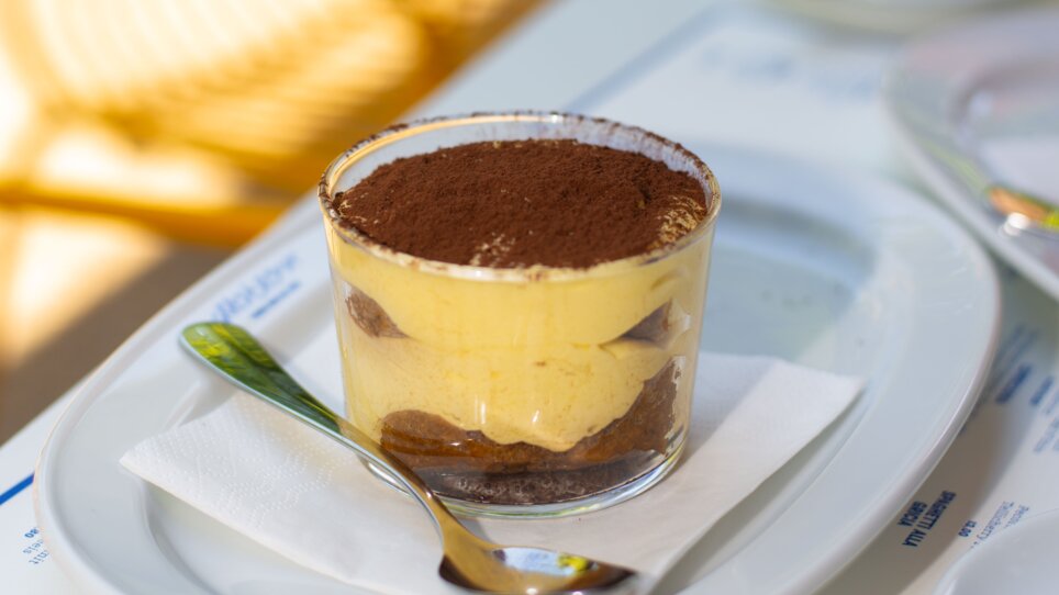 Tiramisu served in a glass with a spoon on a white plate at the Grazie Roma restaurant in the Hotel Daniel in Graz. | © Florian Weitzer Hotels & Restaurants