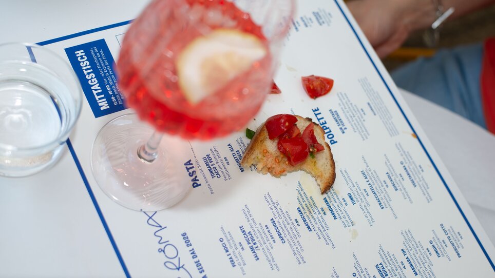 A glass of red aperitif and a piece of bruschetta with a bite taken out of it, pictured on a menu. | © Florian Weitzer Hotels & Restaurants