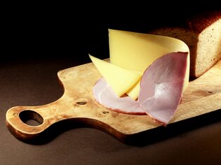 Scheiben von Käse und Schinken mit einem Brot auf einem Holzbrett. | © Sattler