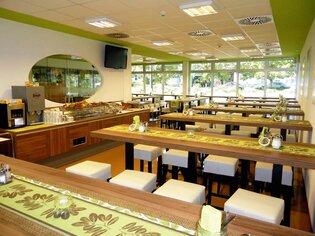 Area di ristorazione moderna con lunghi tavoli in legno e sedie bianche. | © Greenrooms