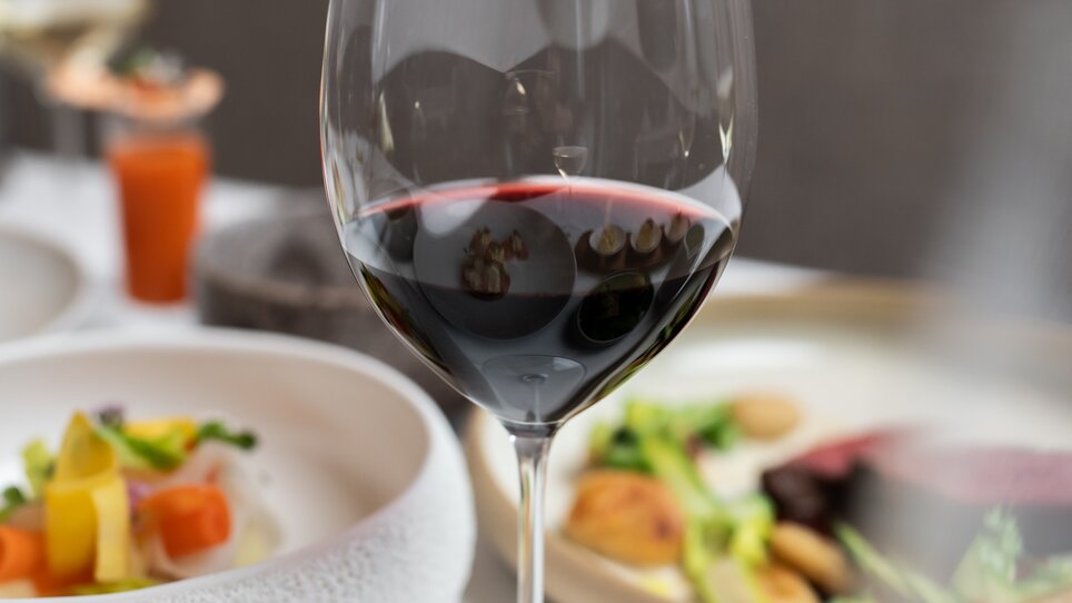 A glass of red wine stands on a beautifully set table with gourmet dishes. | © Studio-Lou - Lukas Elsneg