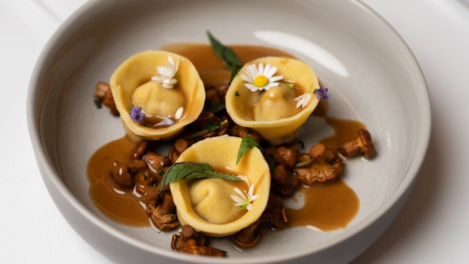 Ein Teller mit Ravioli, Kräutern und Blumen auf Soße. | © Lukas Elsneg