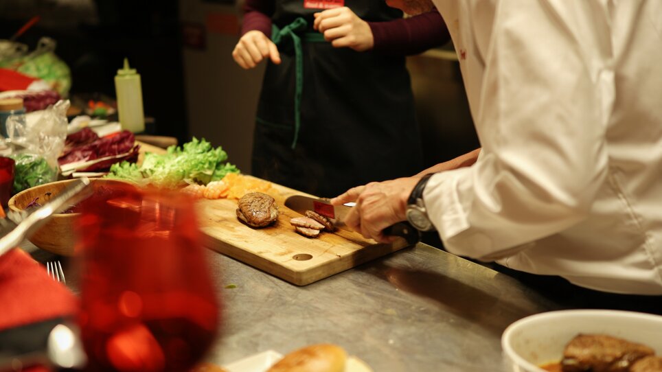 A chef slices meat on a wooden board in a kitchen. | © Makinson Media