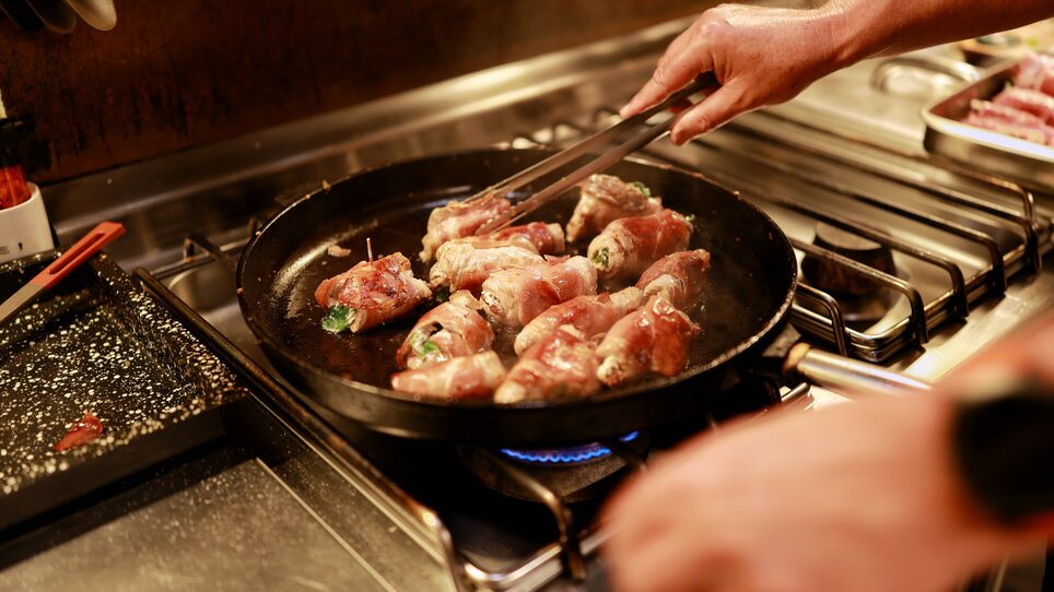 A chef frying stuffed rolls in a pan on the stove. | © Makinson Media