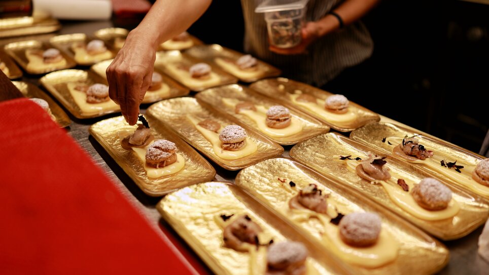 A chef arranges desserts on golden plates. | © Makinson Media
