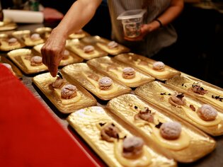 A chef arranges desserts on golden plates. | © Makinson Media