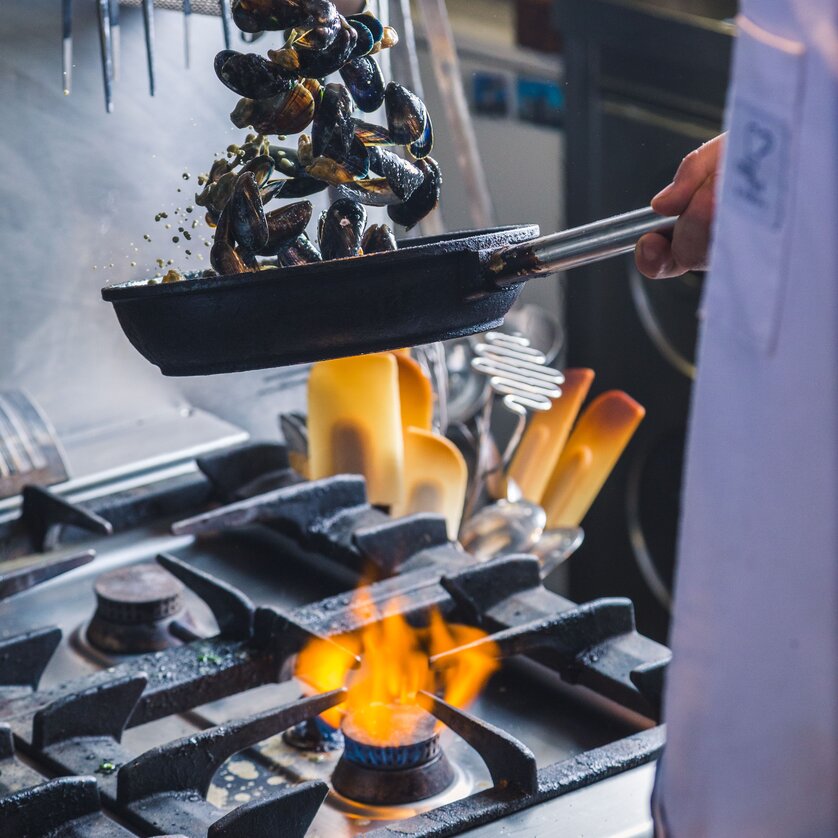 Chef cooking mussels over fire in a kitchen.
