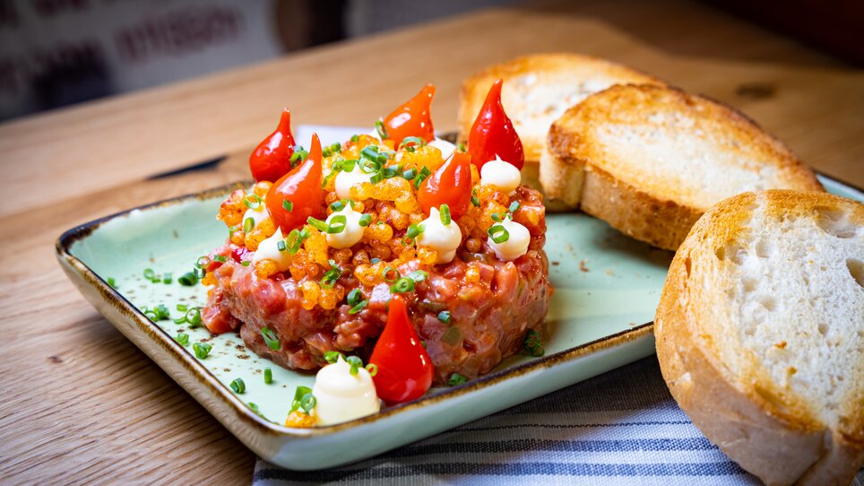 A plate of beef tartare, decorated with tomatoes and chives, served with white bread. | © Kreuzwirt am Rosenberg in Graz