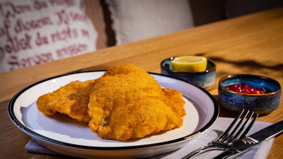 Breaded schnitzel with lemon and cranberries on a plate with cutlery. | © Kreuzwirt am Rosenberg in Graz