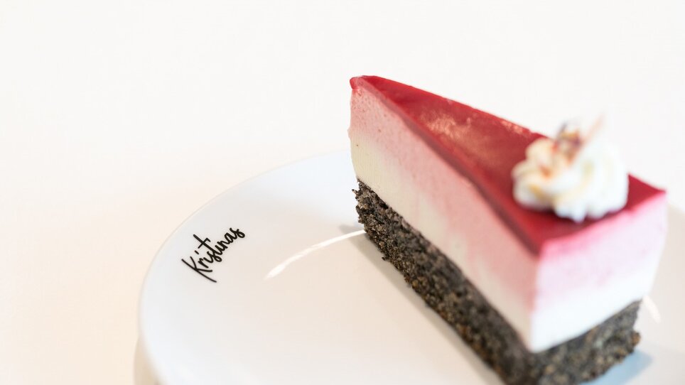 Ein Stück Mohnkuchen mit Topfen und Himbeeren auf einem Teller mit dem Schriftzug "Kristinas".