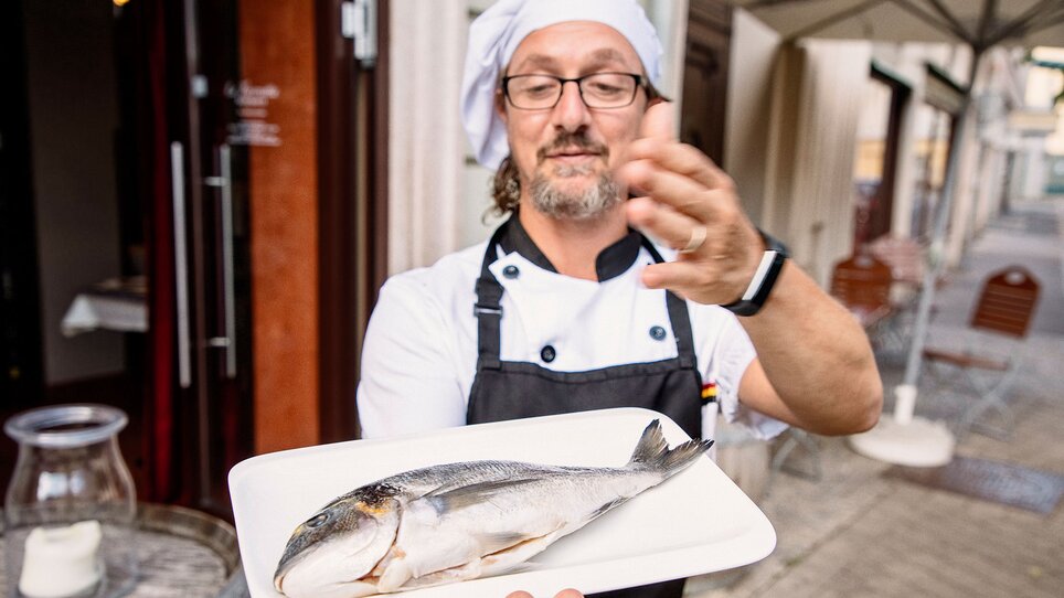 Uno chef mostra un pesce fresco su un piatto davanti al suo ristorante.