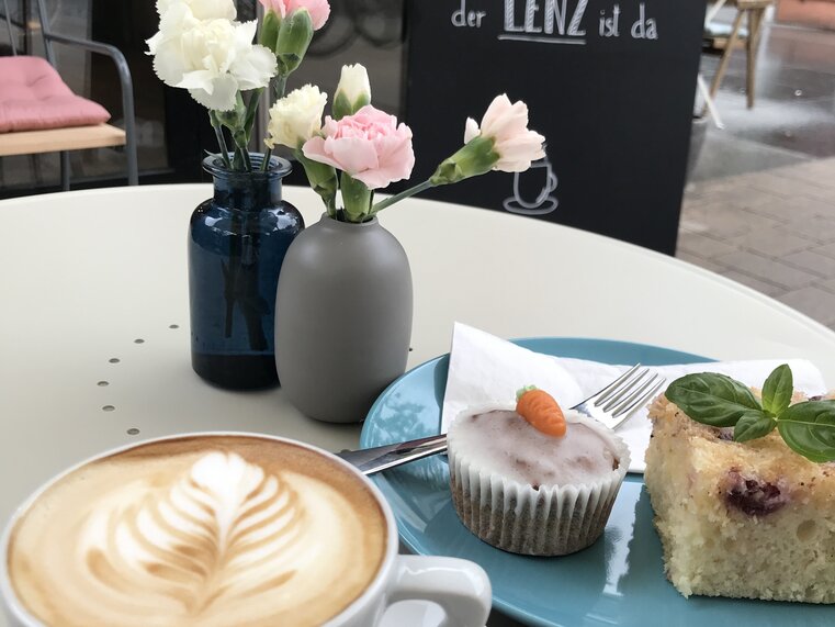 Ein Kaffee, Kuchen und frische Blumen in einem Café.