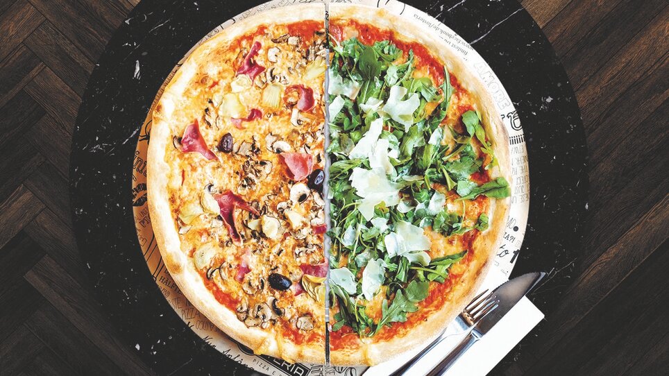 Eine Pizza mit zwei unterschiedlich belegen Seiten. Auf einer Seite ist die Pizza mit Schinken und Champignons belegt und auf der anderen Seite mit Rucola und Parmesan. | © L´Osteria