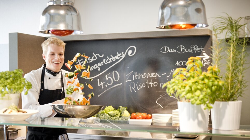 Cuoco sorridente che prepara piatti con verdure fresche. | © Mangolds