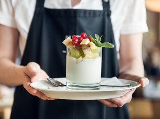 A waiter serves a dessert topped with fresh fruits. | © Martin Auer 
