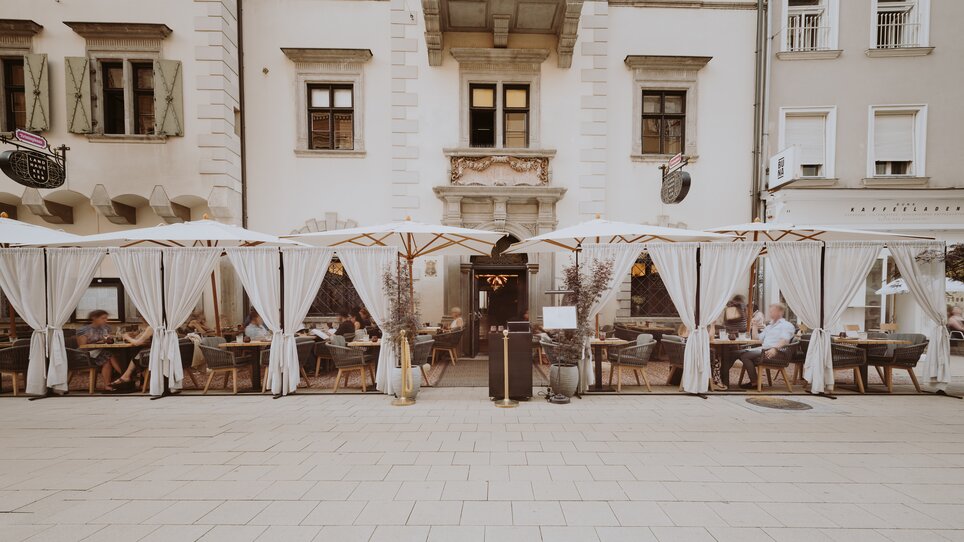 Vista esterna di un ristorante a Graz con posti a sedere sotto tende bianche.