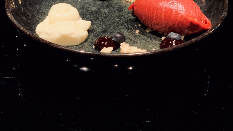 Dessert creativo in una ciotola nera con sorbetto e bacche.