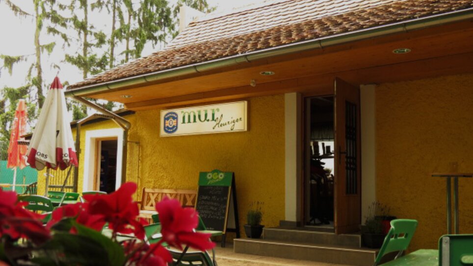 Locale accogliente con facciata gialla e posti a sedere all'aperto, perfetto per mangiare e bere. | © Murheuriger