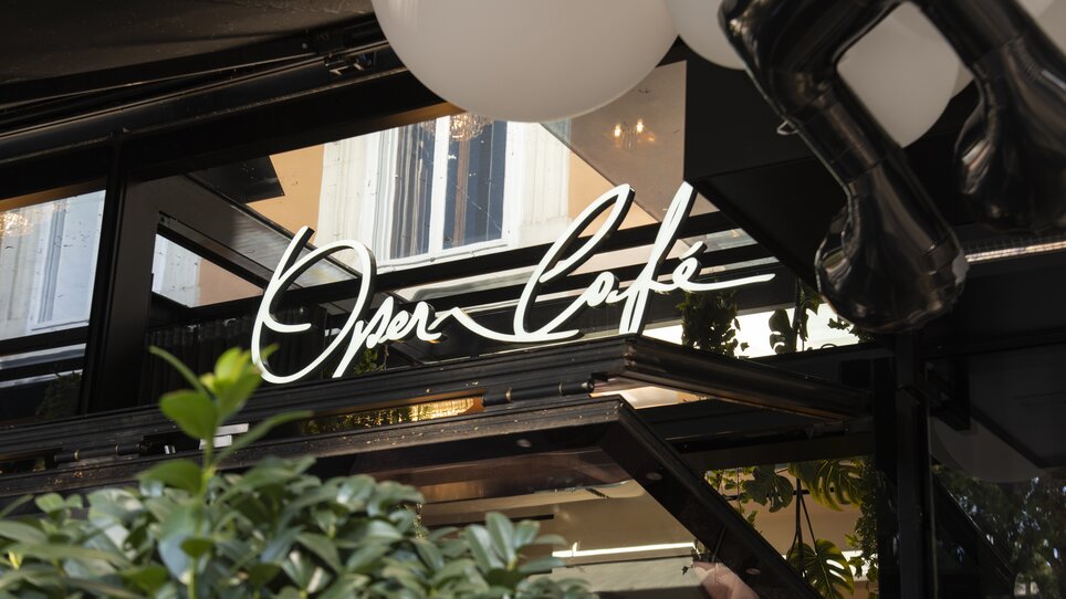 Beleuchtetes Schild des Operncafés mit Pflanzen im Vordergrund. | © Jauk Katharina