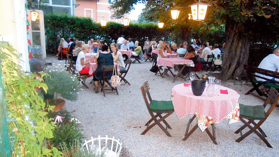 Gemütlicher Gastgarten mit Tischen und Gästen. | © Osteria dei Sensi