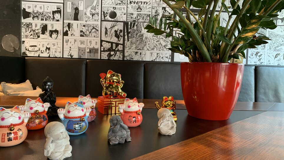 Partial view of a restaurant with lucky figurines and a plant.