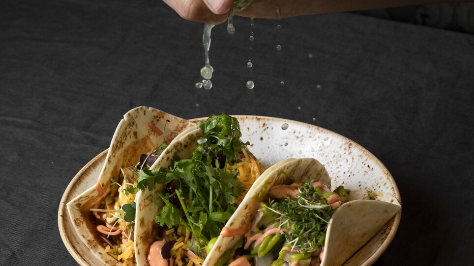 A hand squeezes lime over multiple tacos on a plate. | © Jauk Katharina