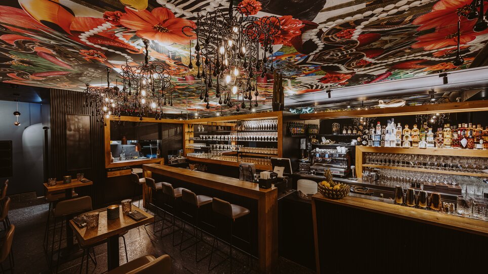 Modern bar with vibrant ceiling design and stylish furniture. | © Joel Kernasenko