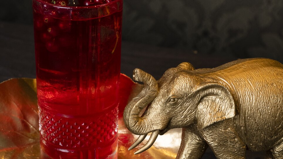 A golden elephant next to a glass of red drink with berries. | © Jauk Katharina